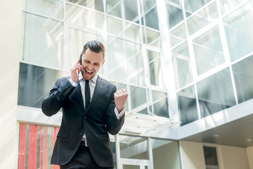 Businessman in a suit celebrating on a phone call after winning a deal
